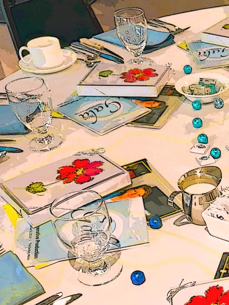 Artist rendering of the dinner table at the 2024 Gala. Items on the table include water glasses, boxes of cards, event programs, and chocolates.