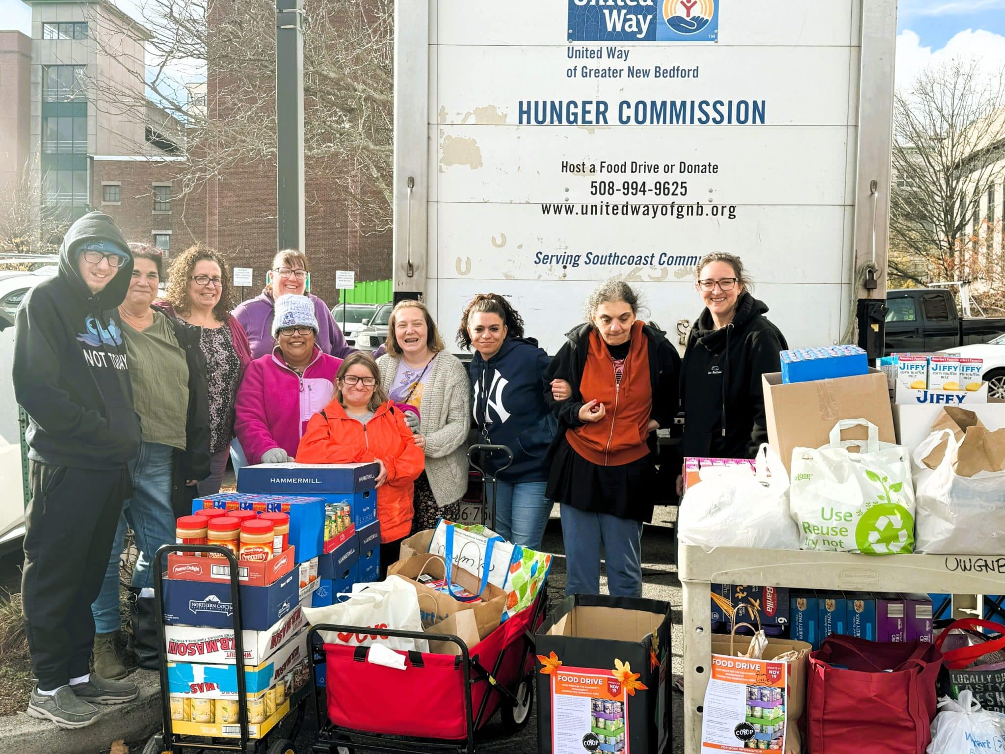 Group of people standing in front of a large truck, surrounded by boxes of food items that are being donated.
